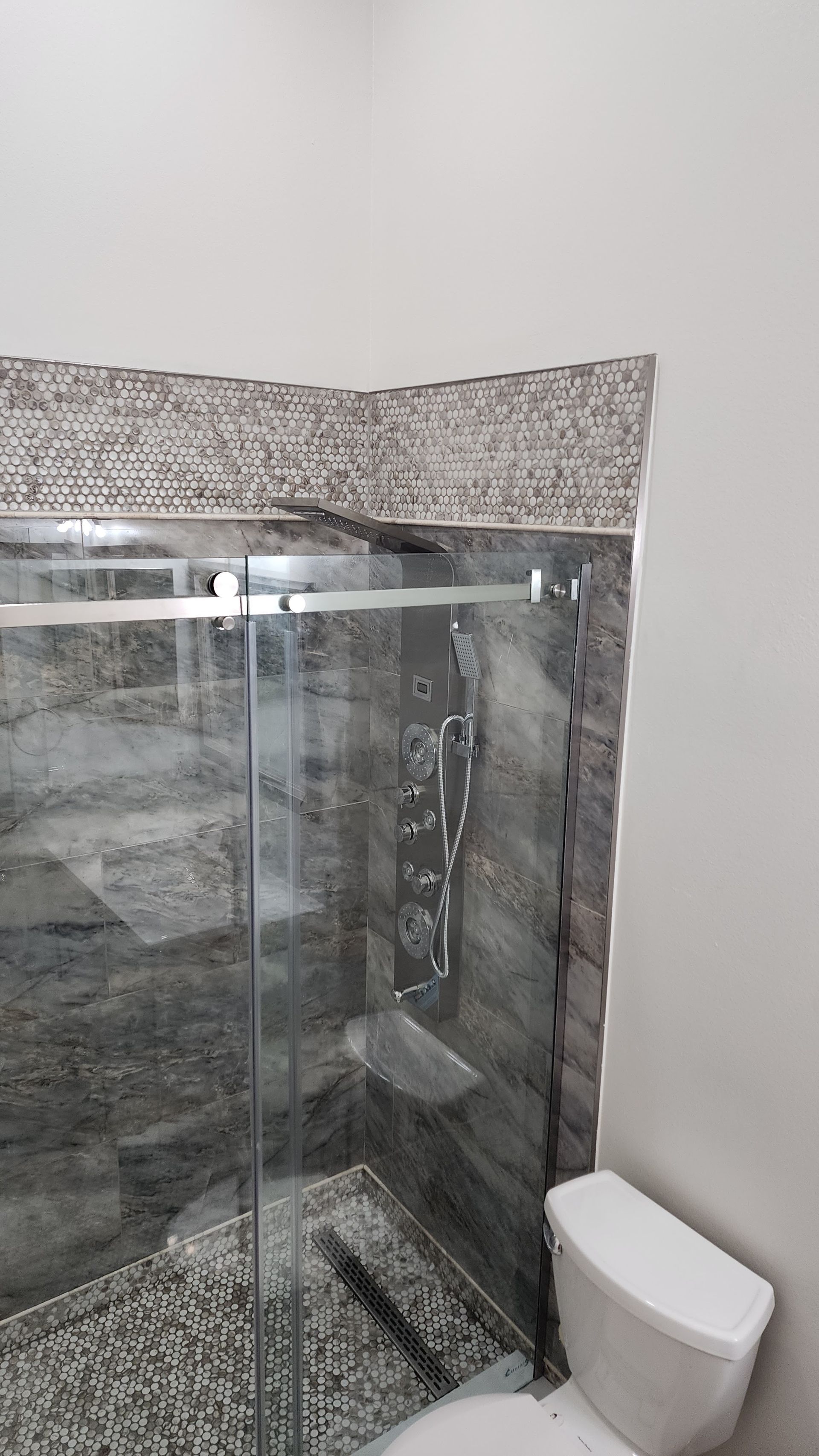 Shower stall with glass door, tiled walls, and a toilet.