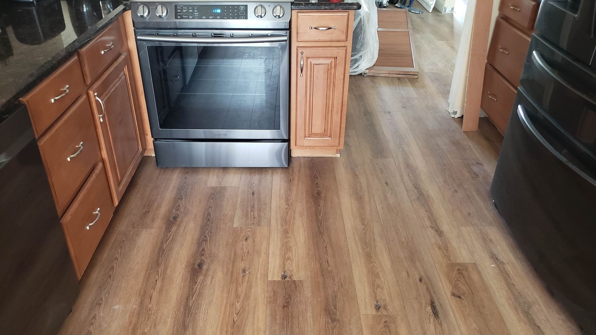 Kitchen with brown wood-look flooring, cabinets, oven, and refrigerator.