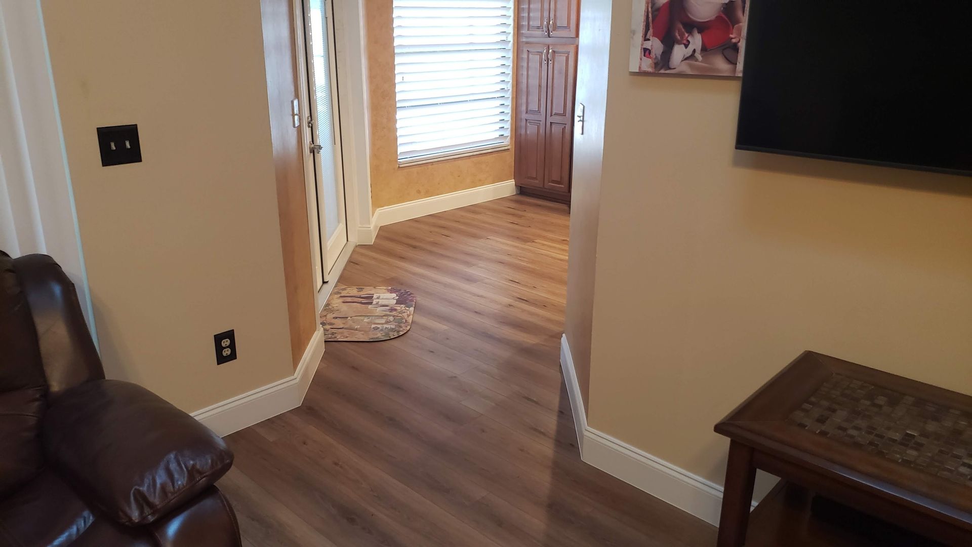 Hallway with wood floors, brown walls, and a door at the end. A recliner is on the left.