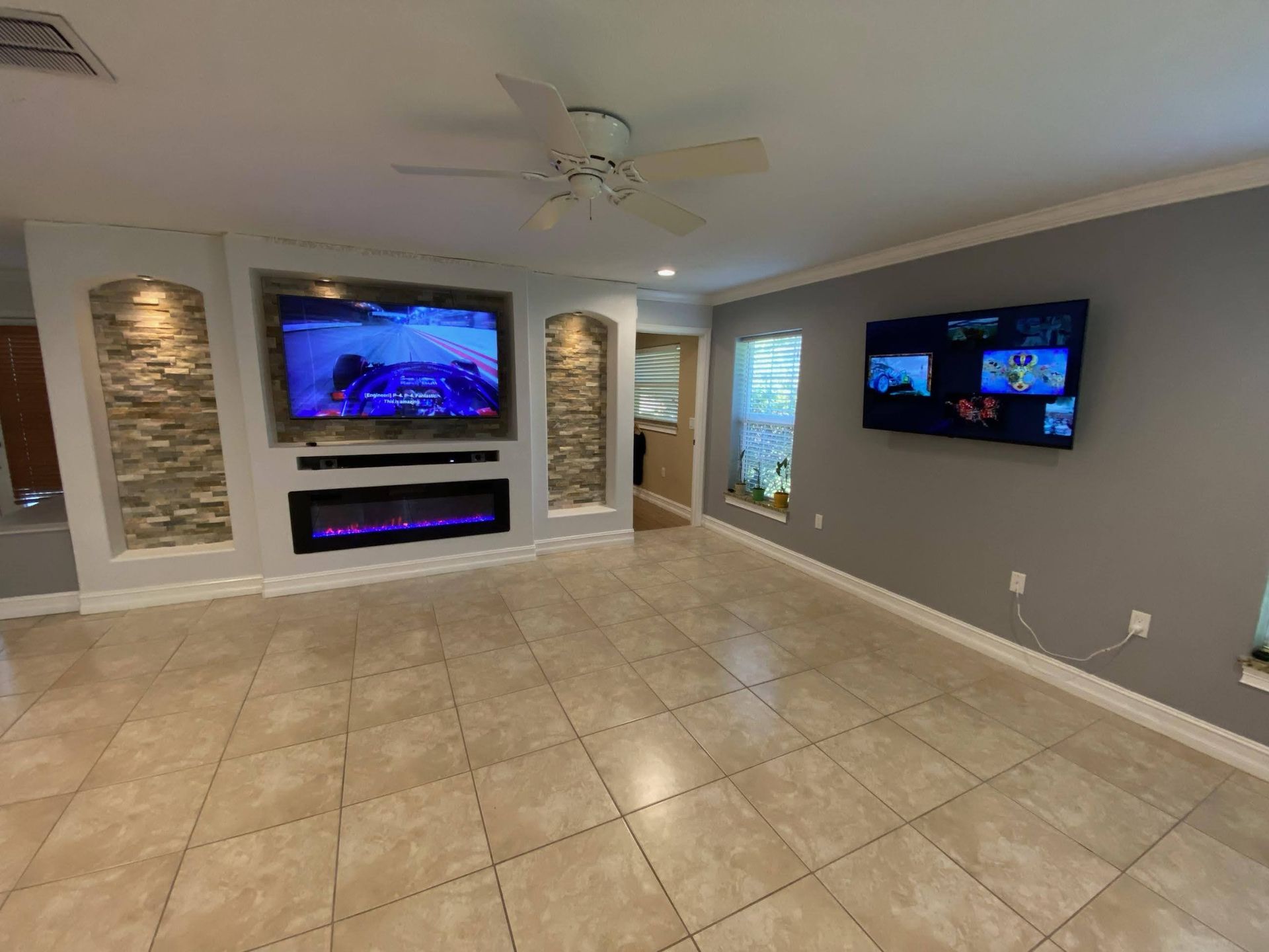 Living room with two mounted TVs, a fireplace, and beige tile floor.