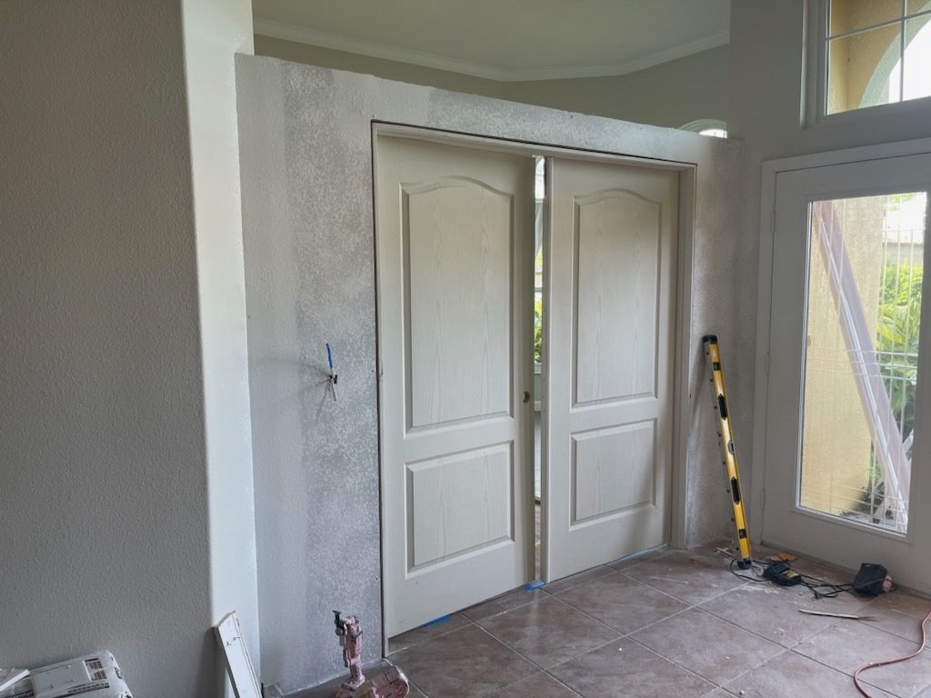 Double doors with light-colored panels set in a doorway with neutral-toned walls; level tool in foreground.