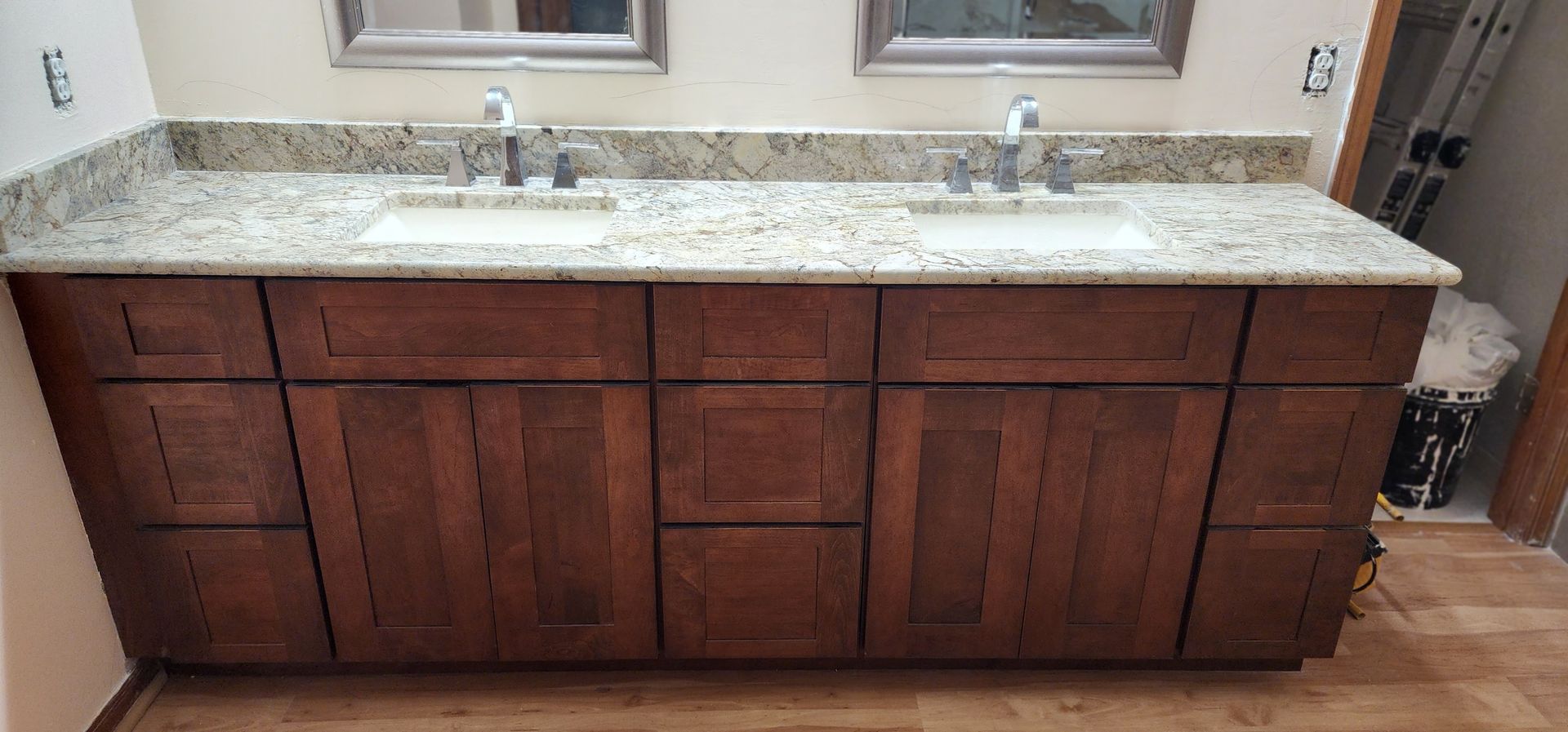 Bathroom vanity with brown cabinets, light-colored granite countertop, and two sinks.