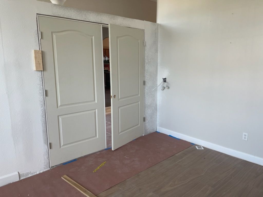 Double doors, one slightly ajar, in a room under construction, with flooring partially installed.