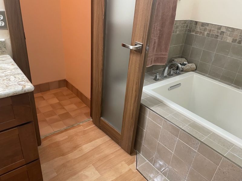 Bathroom with a tub, frosted glass shower door, and wood-look tile flooring.