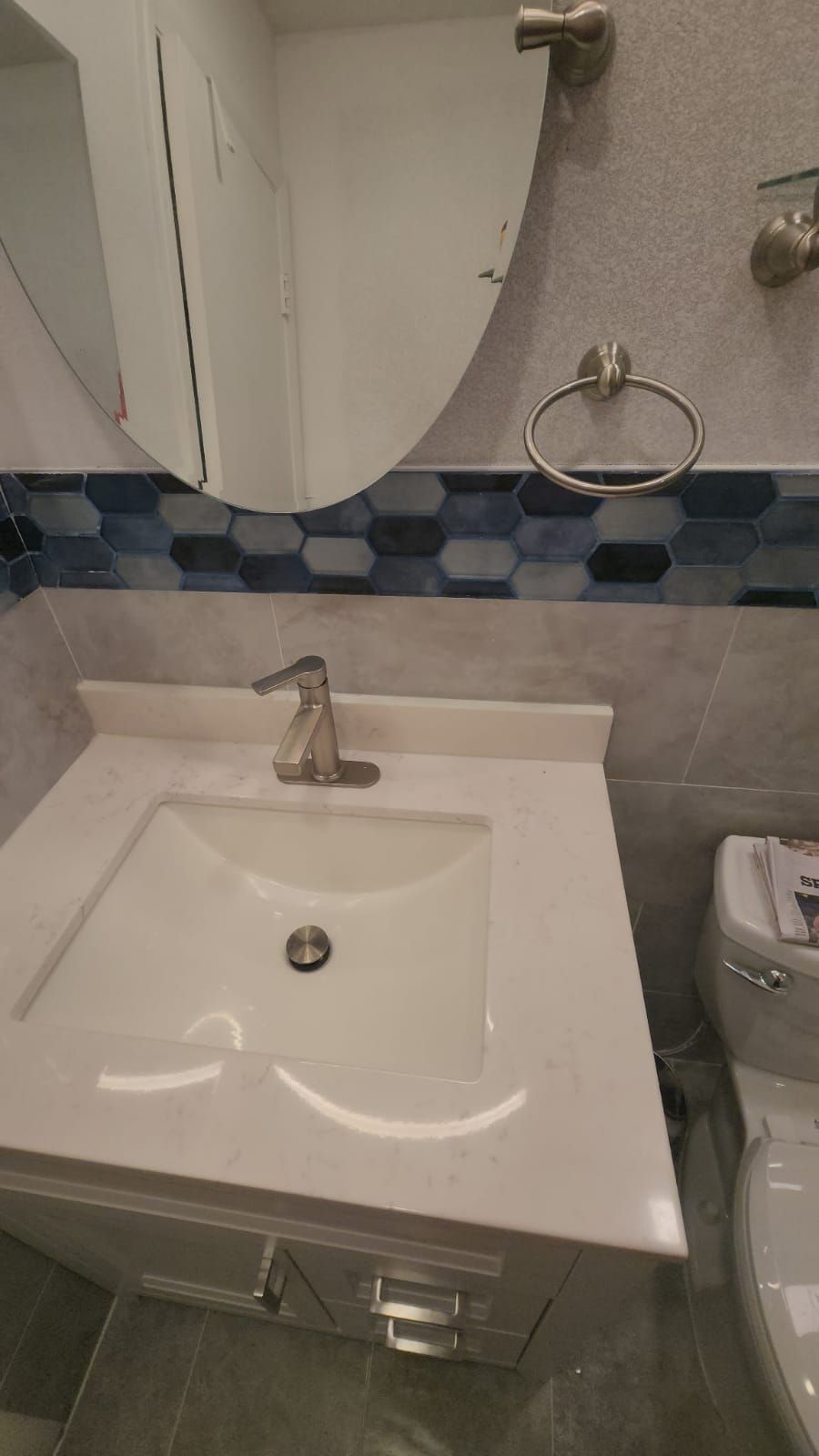 Bathroom vanity with sink, mirror, and towel ring. White countertop, blue tile accent, neutral tones.