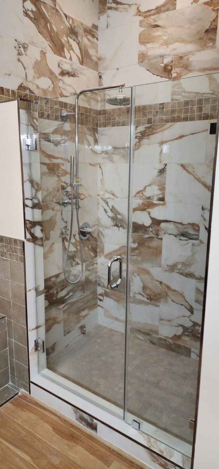 Shower stall with marble-patterned tile, glass doors, and chrome hardware.