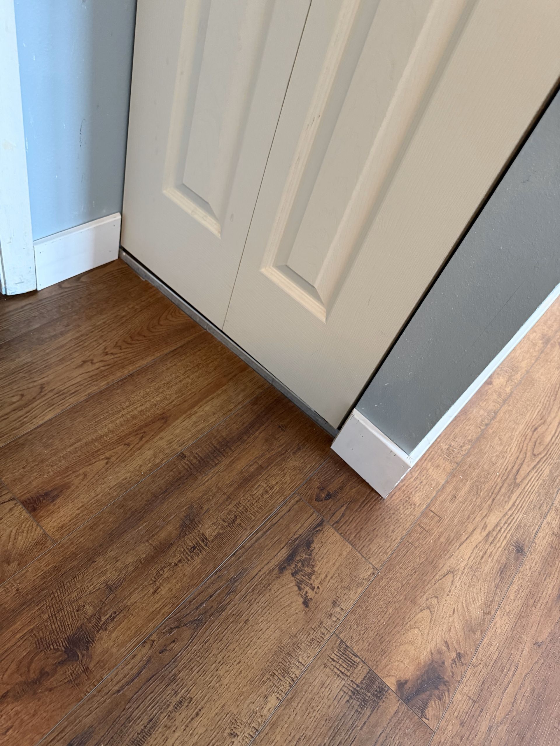 White door slightly ajar on a laminate floor, with white trim and blue and gray walls.