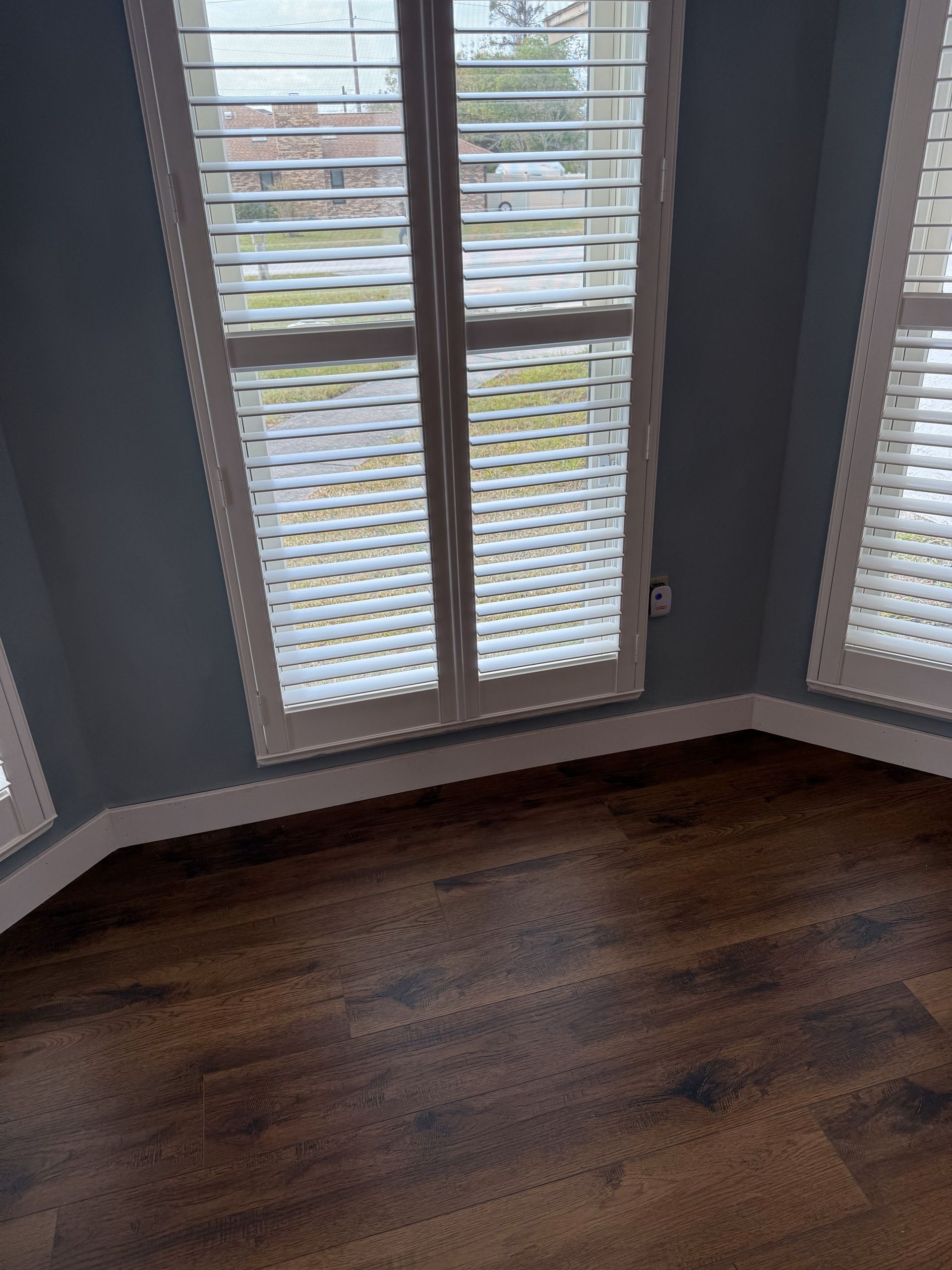 Room corner with wood floor, blue walls, and windows with white shutters.