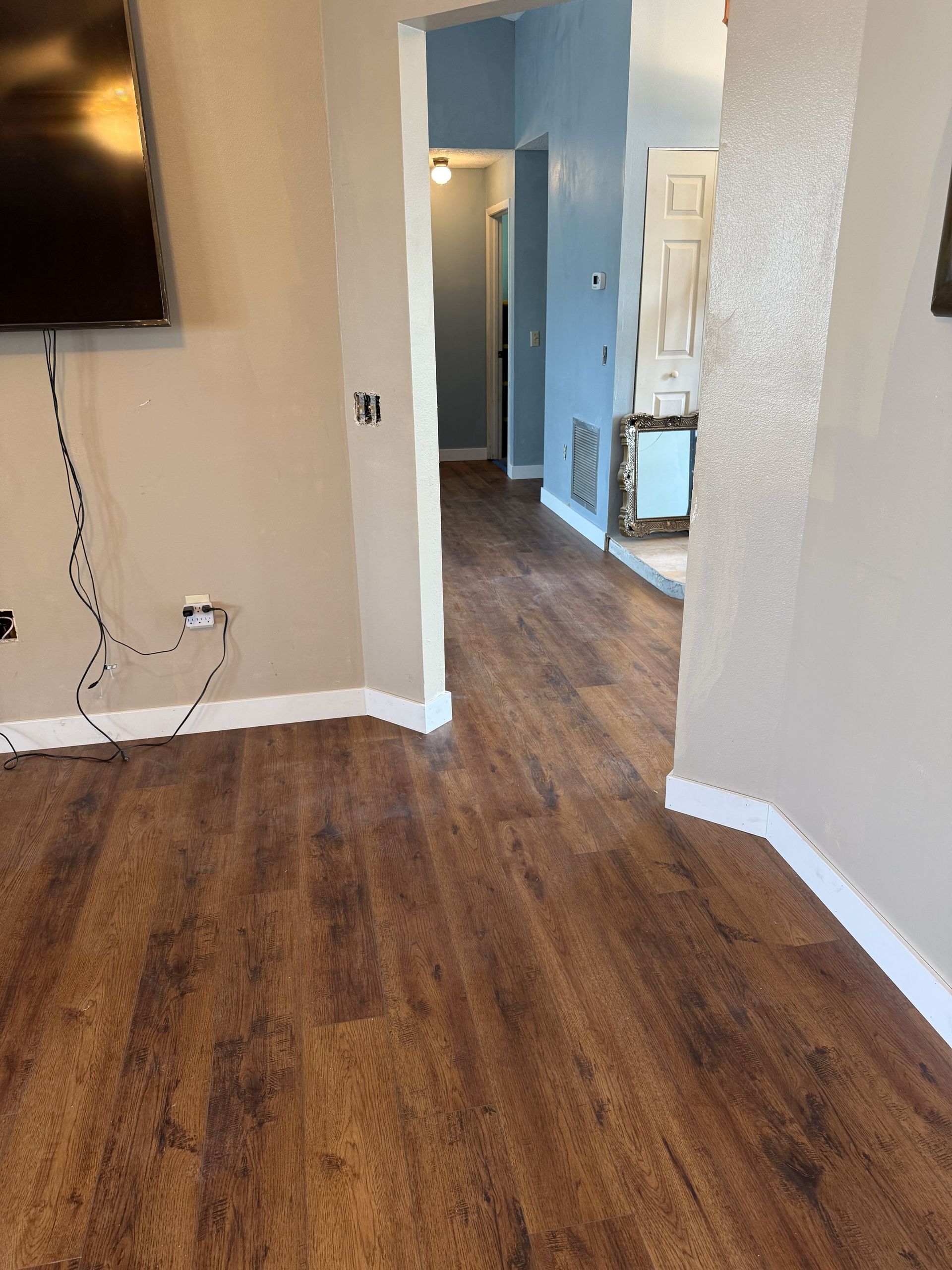 Wooden floors lead to hallway with blue walls and doorway. Cream trim and walls.