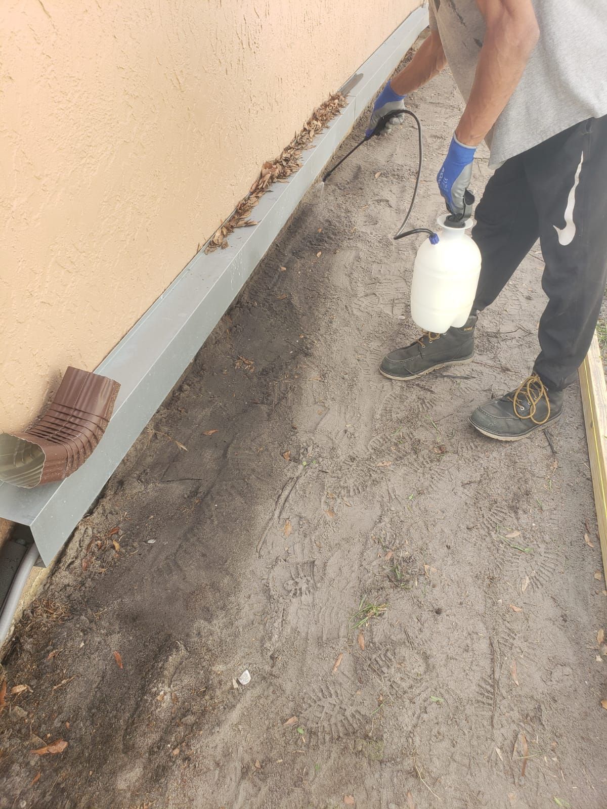 Person spraying a concrete walkway next to a building.