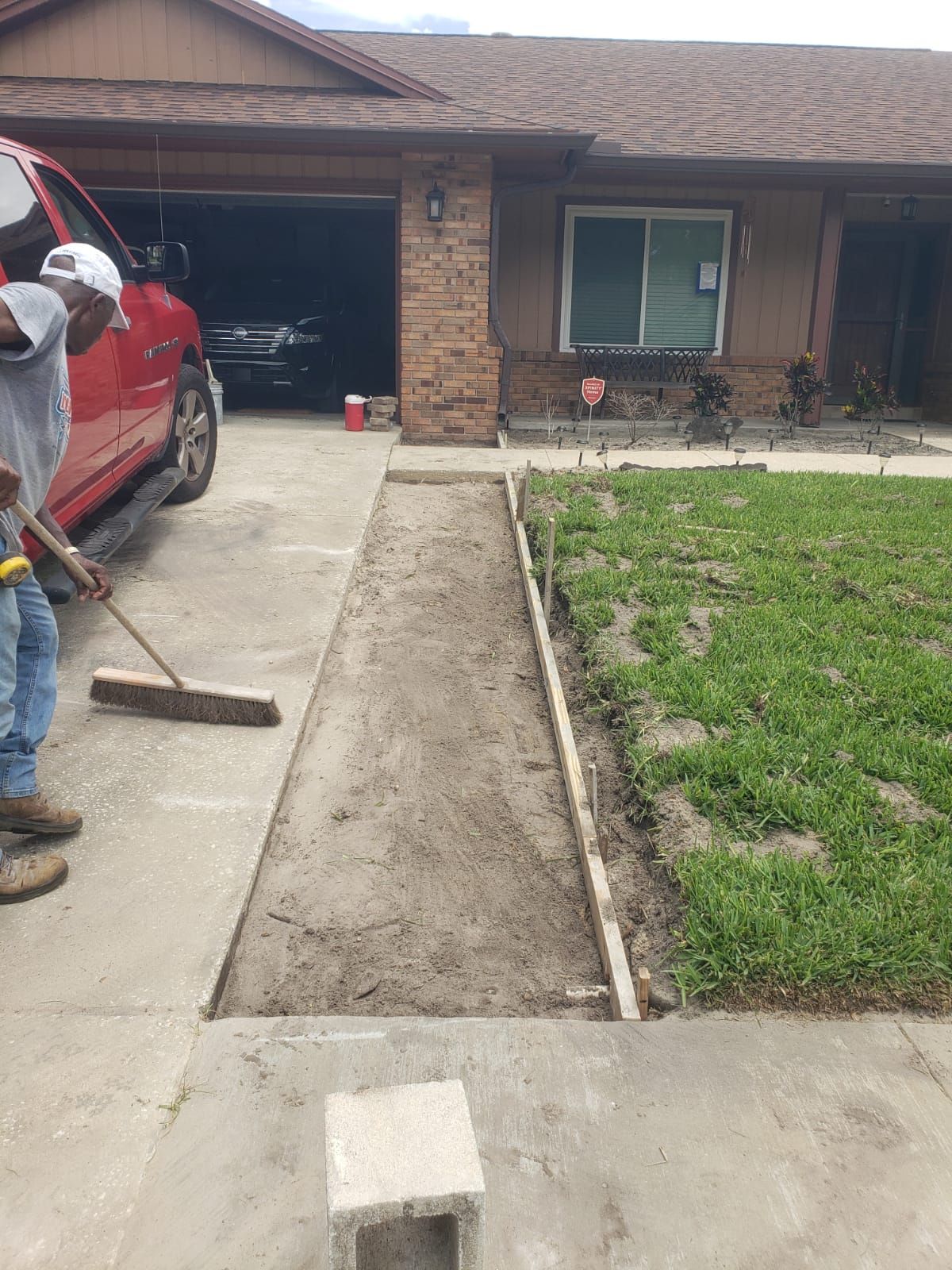 Man sweeping dirt from a concrete walkway, likely preparing for installation, in front of a house.