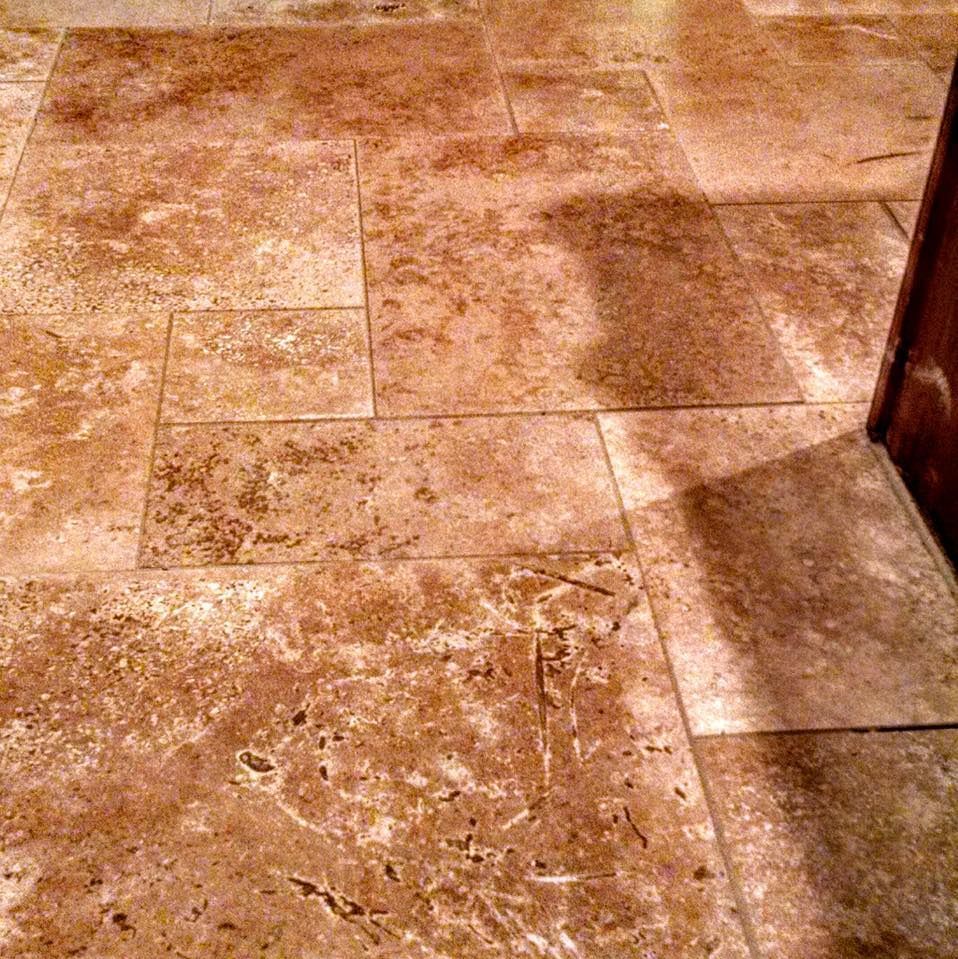 Brown and beige travertine tile floor, different rectangular sizes, next to a wood door.