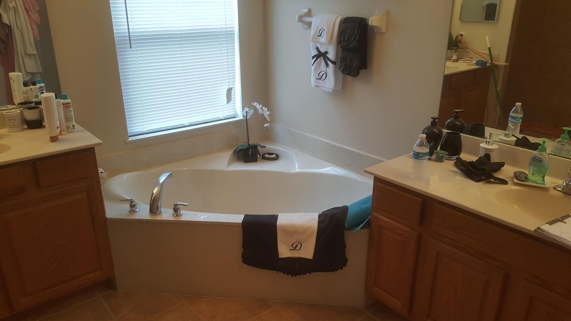 Bathroom with corner bathtub, two vanities, window with blinds, and towels.