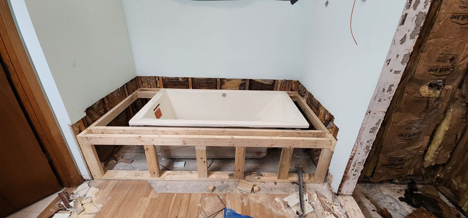 Bathtub in framed wood platform. Room walls damaged, debris on floor.