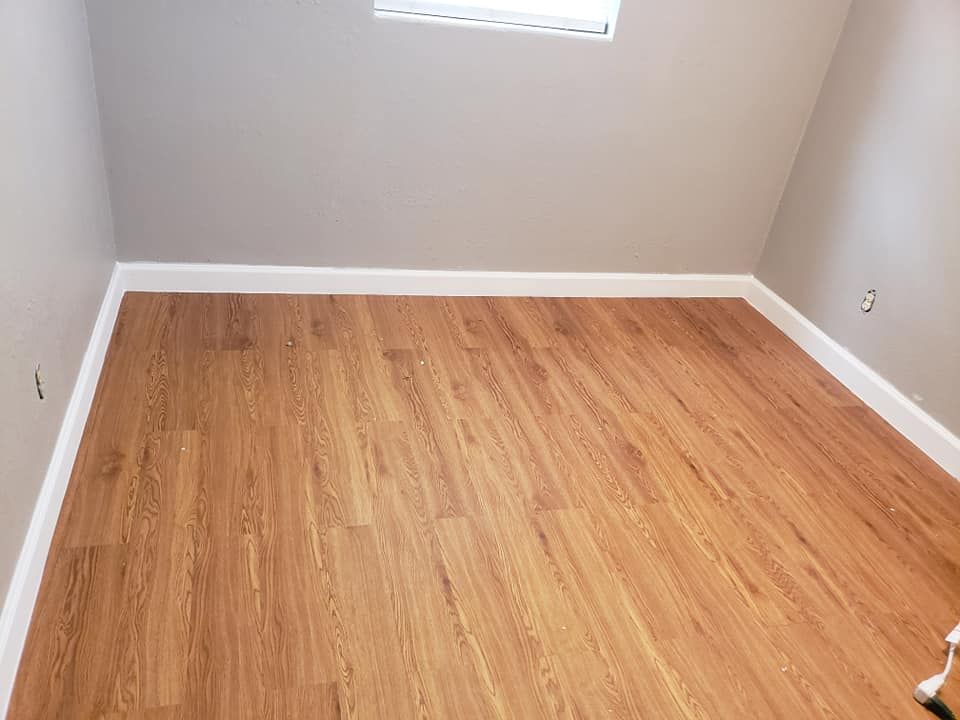 Empty room with wood-look flooring, gray walls, white baseboards, and a small window.