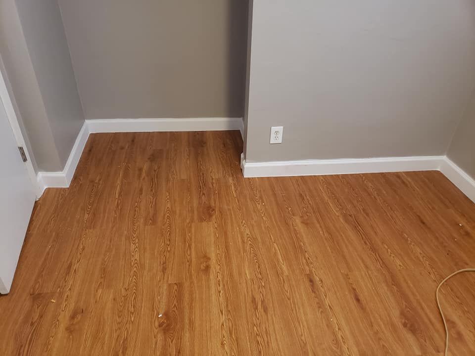 Wooden floor in a room with white baseboards and gray walls; electrical outlet visible.