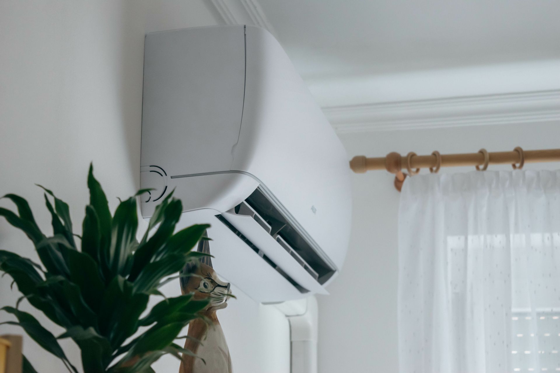 a white air conditioner is hanging from the ceiling in a living room next to a plant .