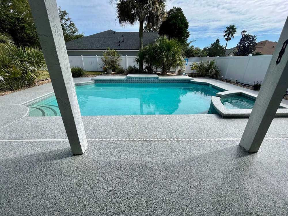 Poolside view with turquoise water, a hot tub, and gray concrete deck. White fence and blue sky.