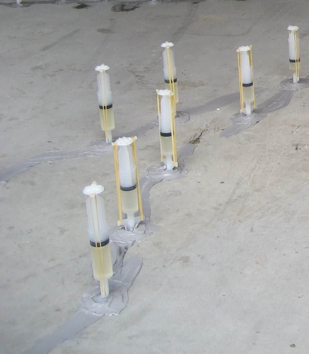 Syringes fixed to a concrete crack, sealed with mortar and held by rubber bands.
