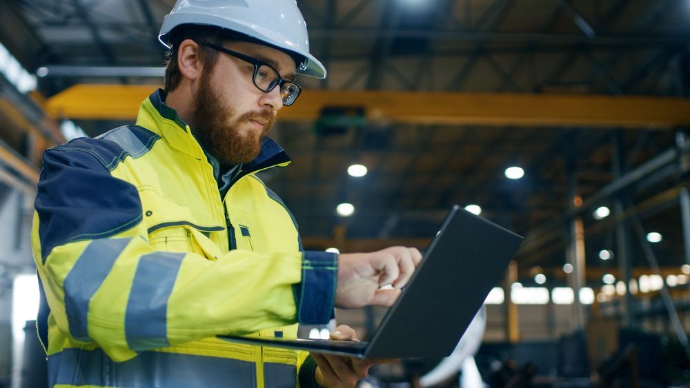 Un hombre con casco utiliza una computadora portátil en una fábrica.