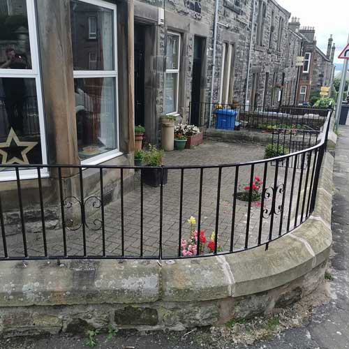 Black railing on brick wall with row of houses in background