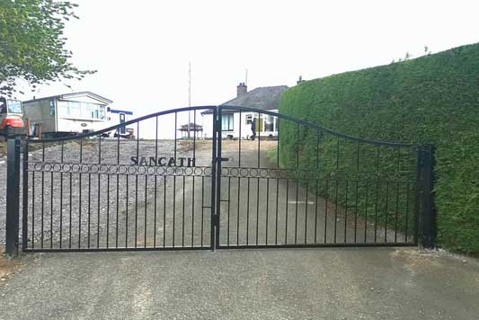 Bespoke black gate, concrete path, green hedges and a caravan and bungalow in the background