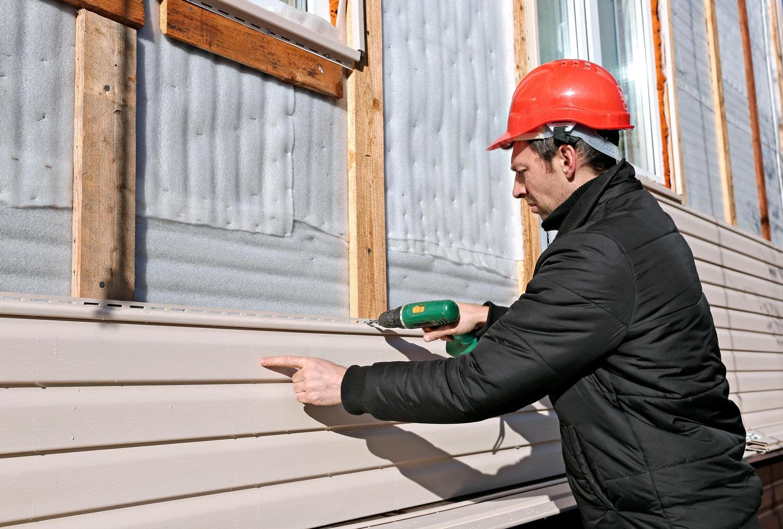 Person in hard hat using a drill to install siding on a building.