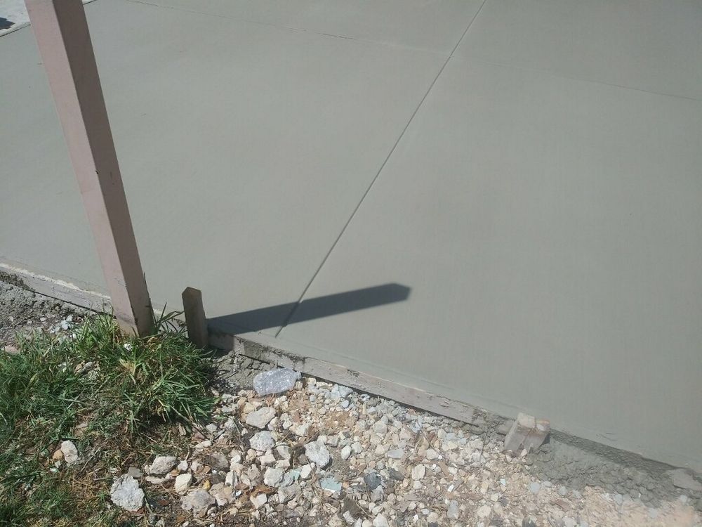 Freshly poured concrete surface next to a wooden form, string guide, and grassy area.