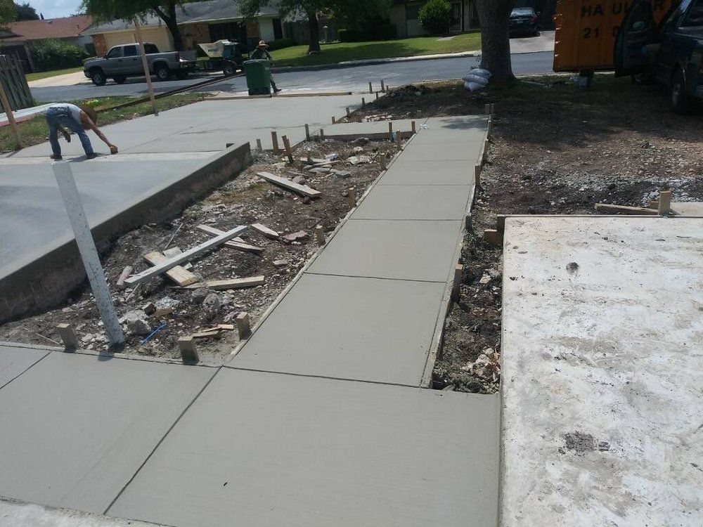 Concrete sidewalk construction in progress; worker smoothing wet cement.