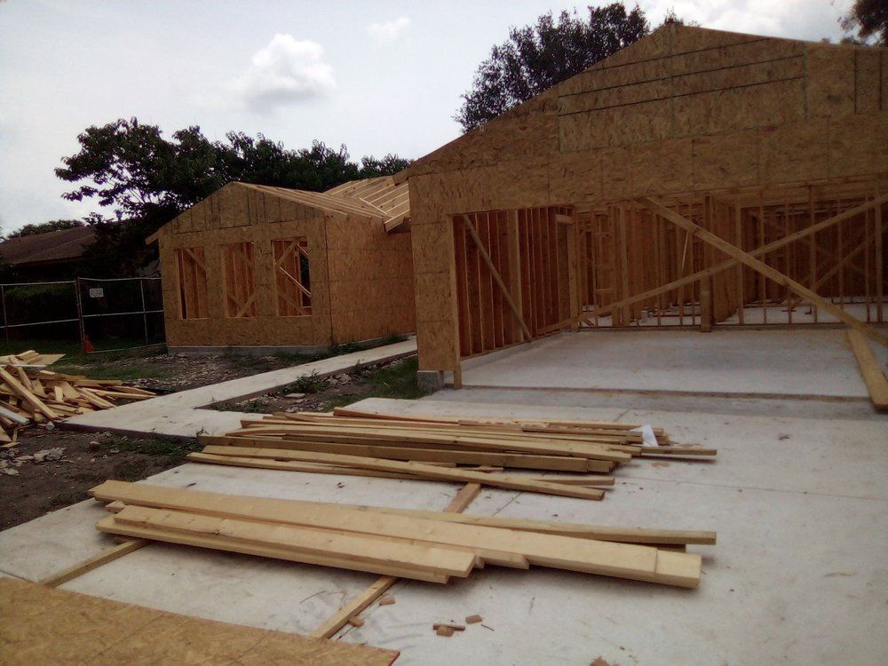 House under construction; wooden frame visible. Garage area and building materials are present. Concrete slab.