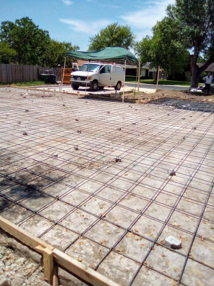 Concrete foundation grid prepared for pouring. White van parked nearby under shade. Sunny day.