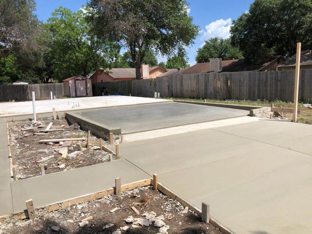 Concrete slab and driveway under construction in a backyard, surrounded by wood framing.
