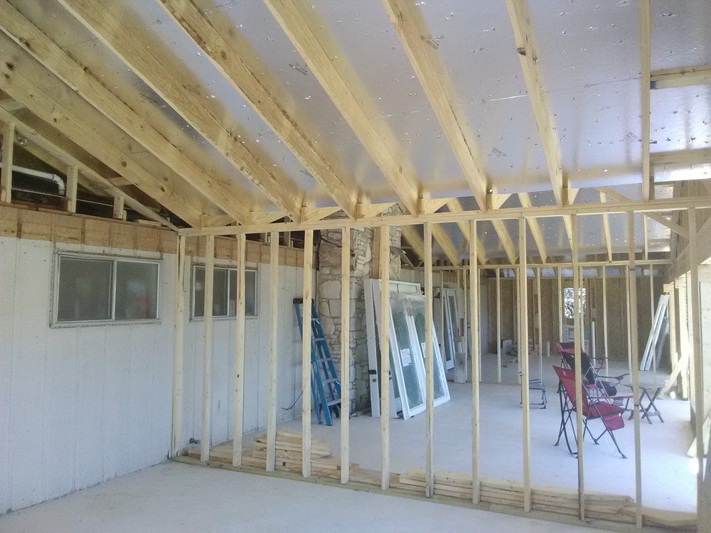 Interior of a room under construction, with wooden framing, windows, and exposed ceiling beams.
