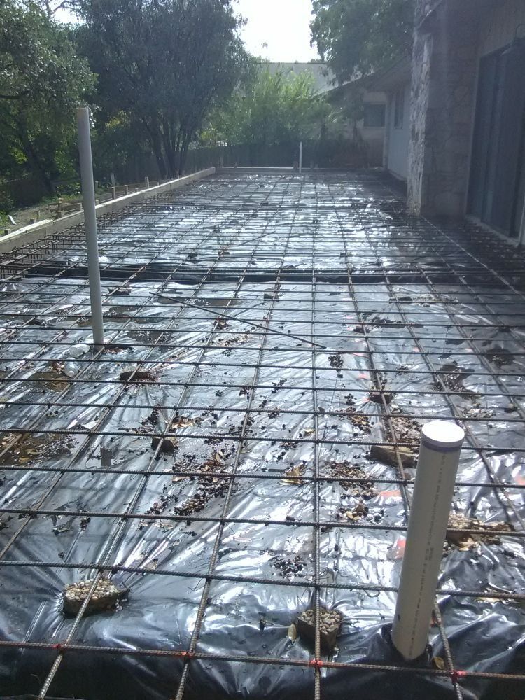 Construction site: metal rebar grid laid over black plastic, ready for concrete.  PVC pipes rise vertically.