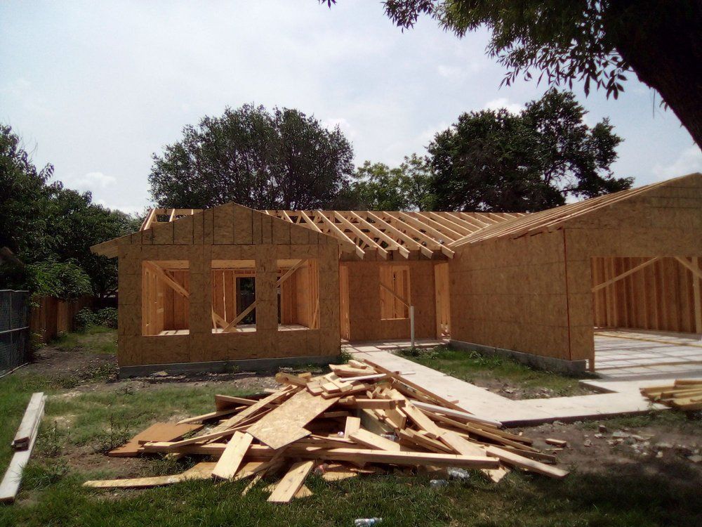 House under construction; wood frame, exposed beams, and OSB sheathing on a sunny day.