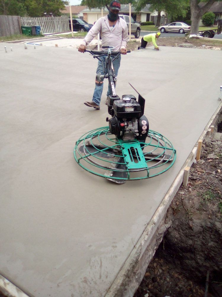 Man using a concrete power trowel on a newly poured concrete slab; outdoor construction site.