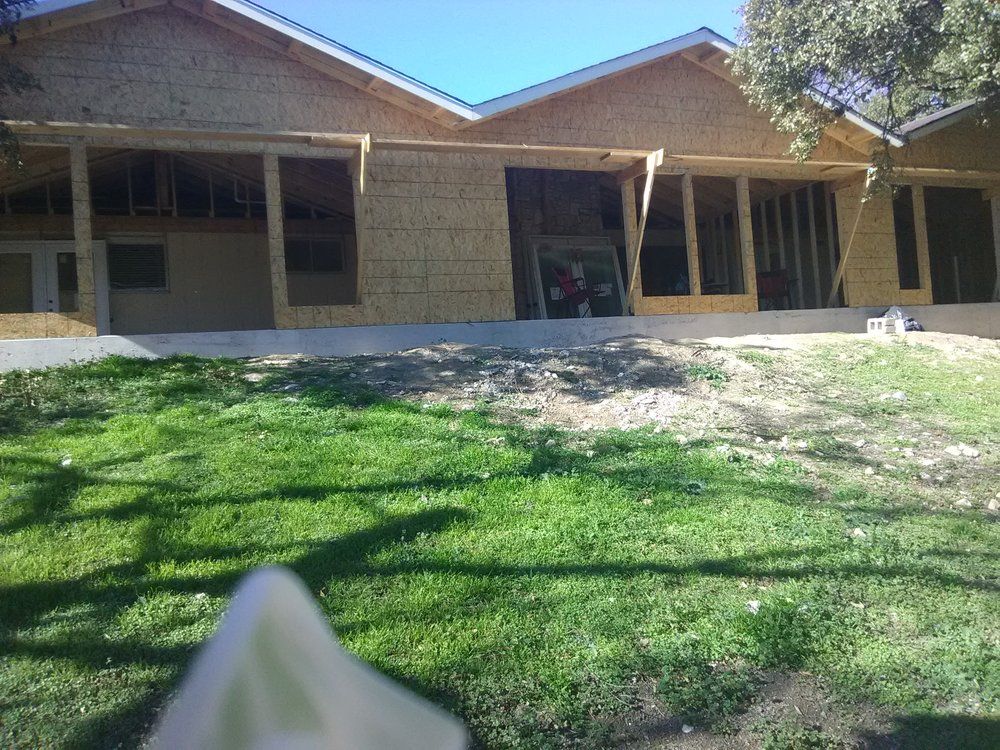 Construction site; unfinished house with wooden frame and siding, on a grassy hill under a blue sky.