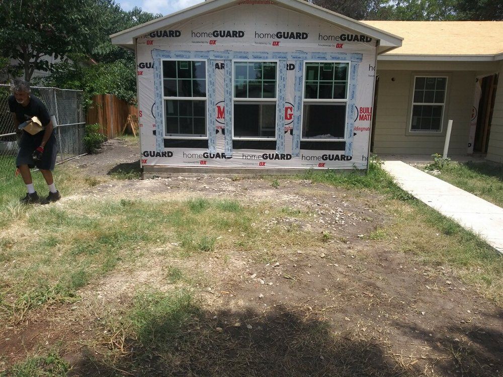 Construction of a house with three windows. A person carries materials on the lawn.