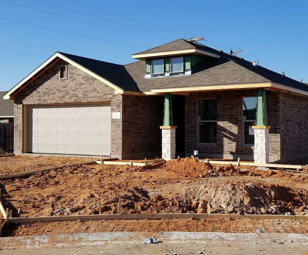 New house under construction, brick exterior, garage door, dirt yard.