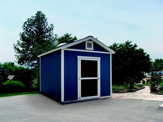 Blue storage shed with white trim and screen door, on a paved surface, trees in background.