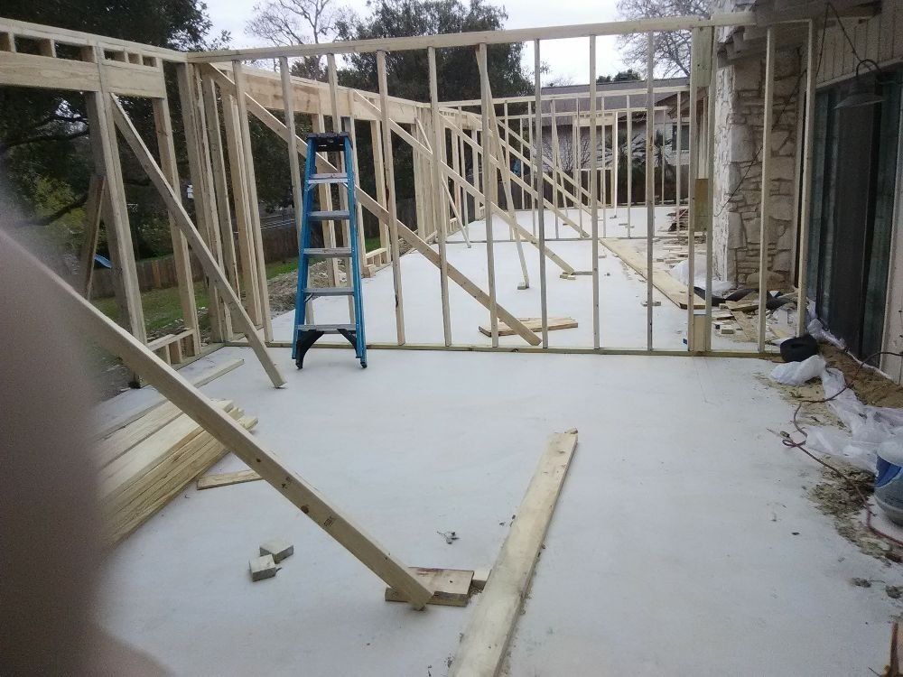 Wooden framework construction on a concrete patio. A blue ladder stands inside the frame.