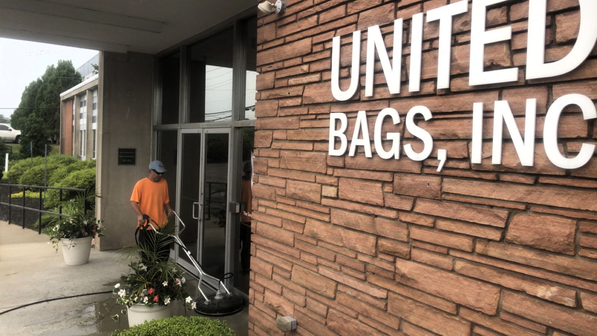 A man power washes the entrance of United Bags, Inc., a brick building with white lettering.