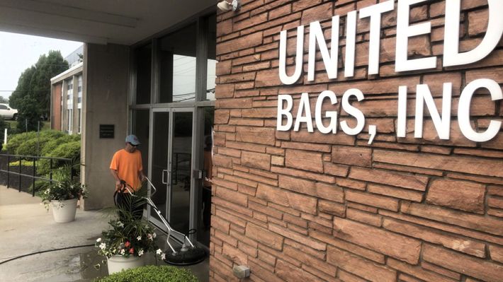 A man power washes the entrance of United Bags, Inc., a brick building with white lettering.