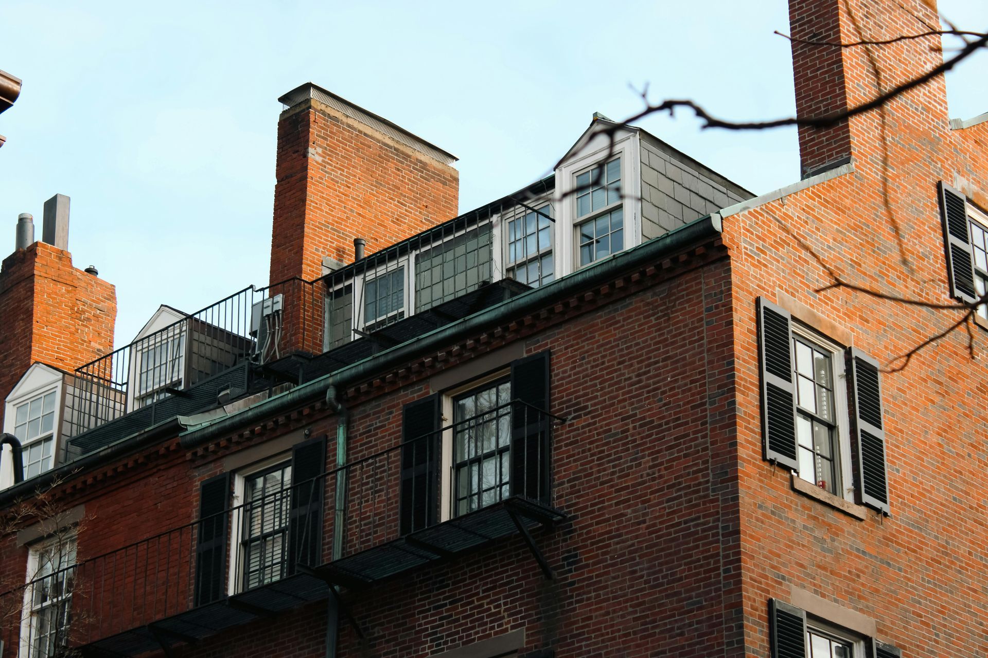 Red brick buildings with multiple windows and rooftop structures against a pale blue sky.