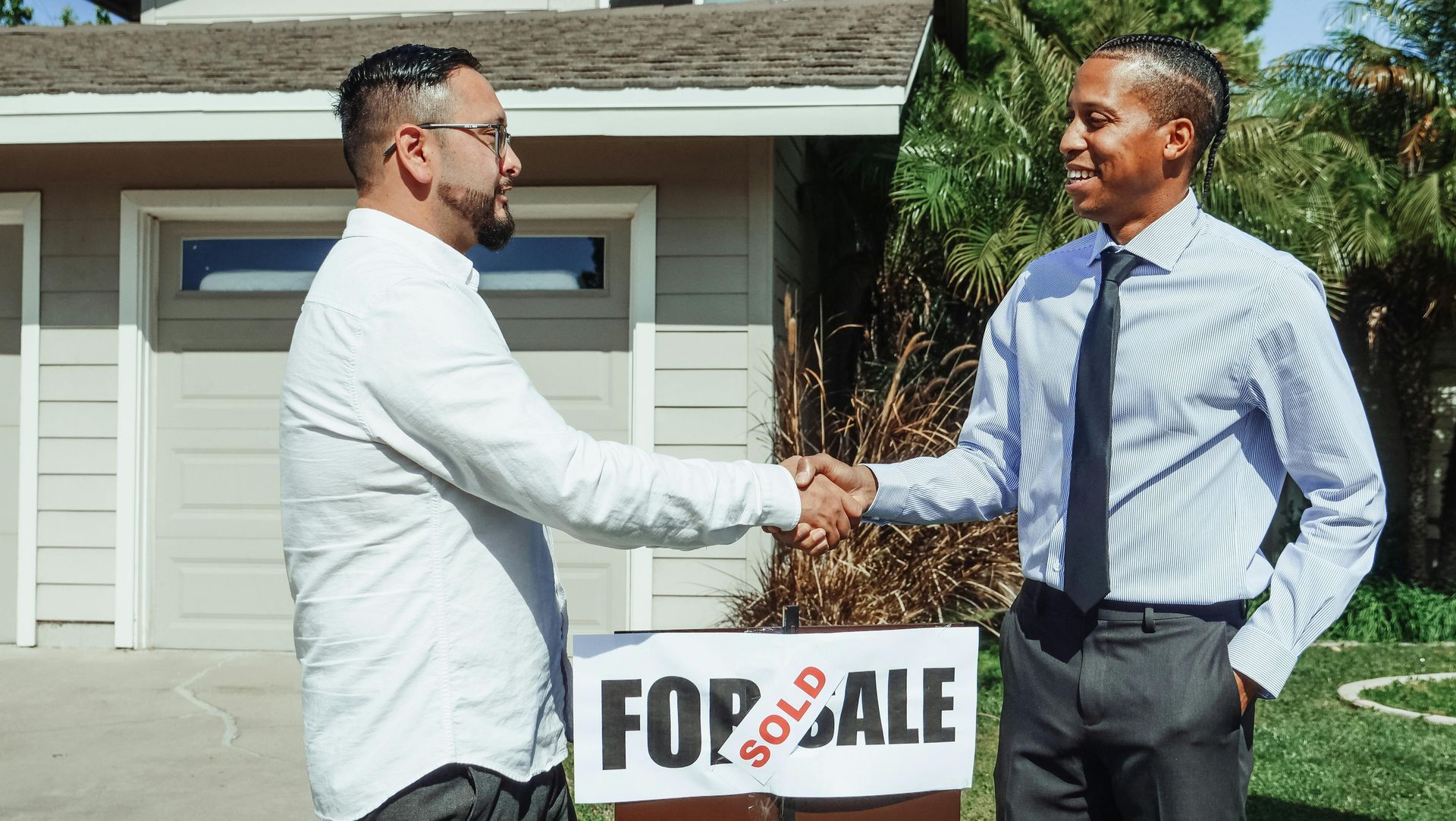 Two men shaking hands in front of a house; a