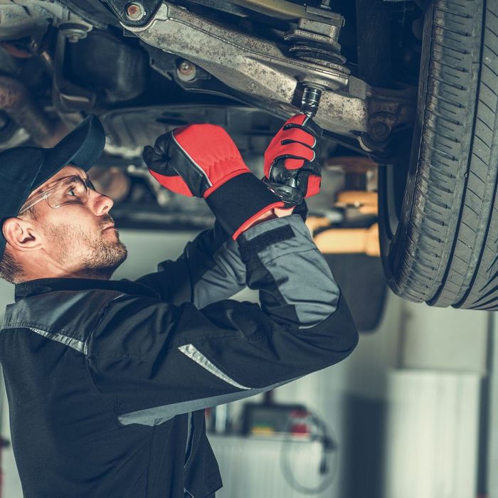 A man is working on the underside of a car in a garage.