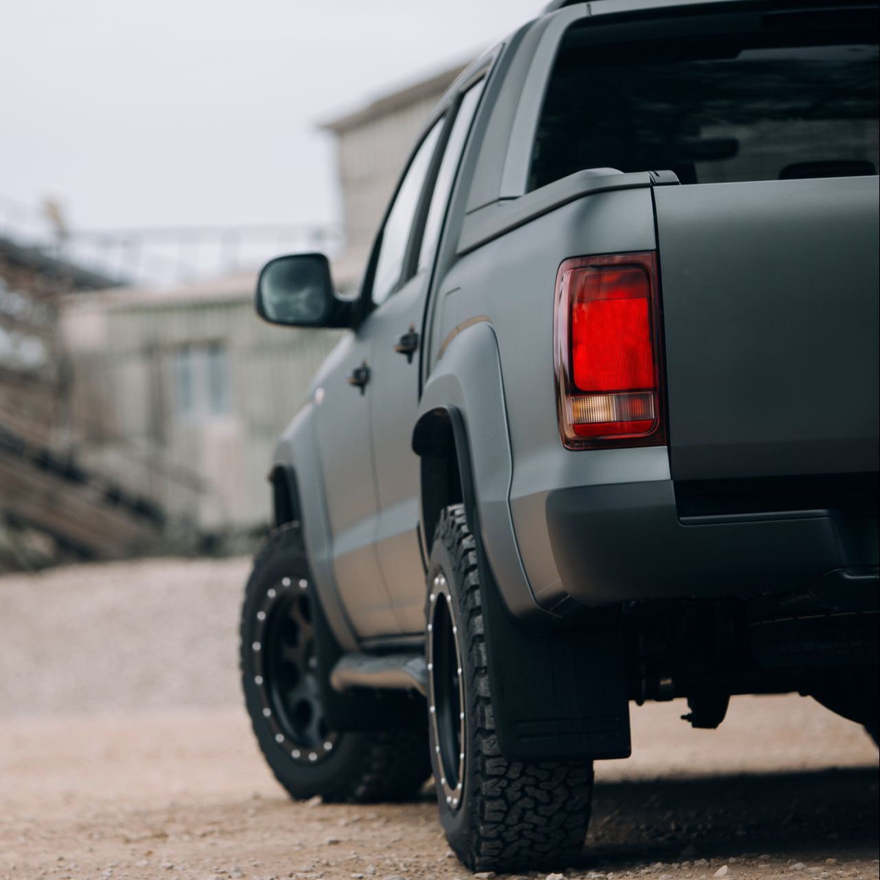 A gray truck with a red tail light is parked on a dirt road