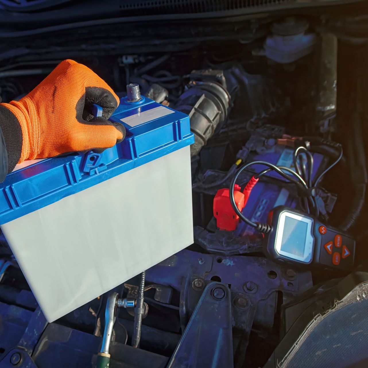 A person is holding a blue and white battery under the hood of a car.