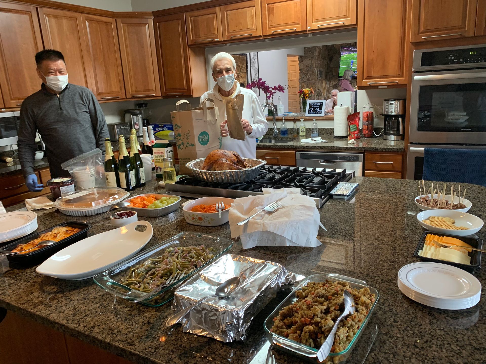 Two men wearing face masks are standing in a kitchen preparing food.