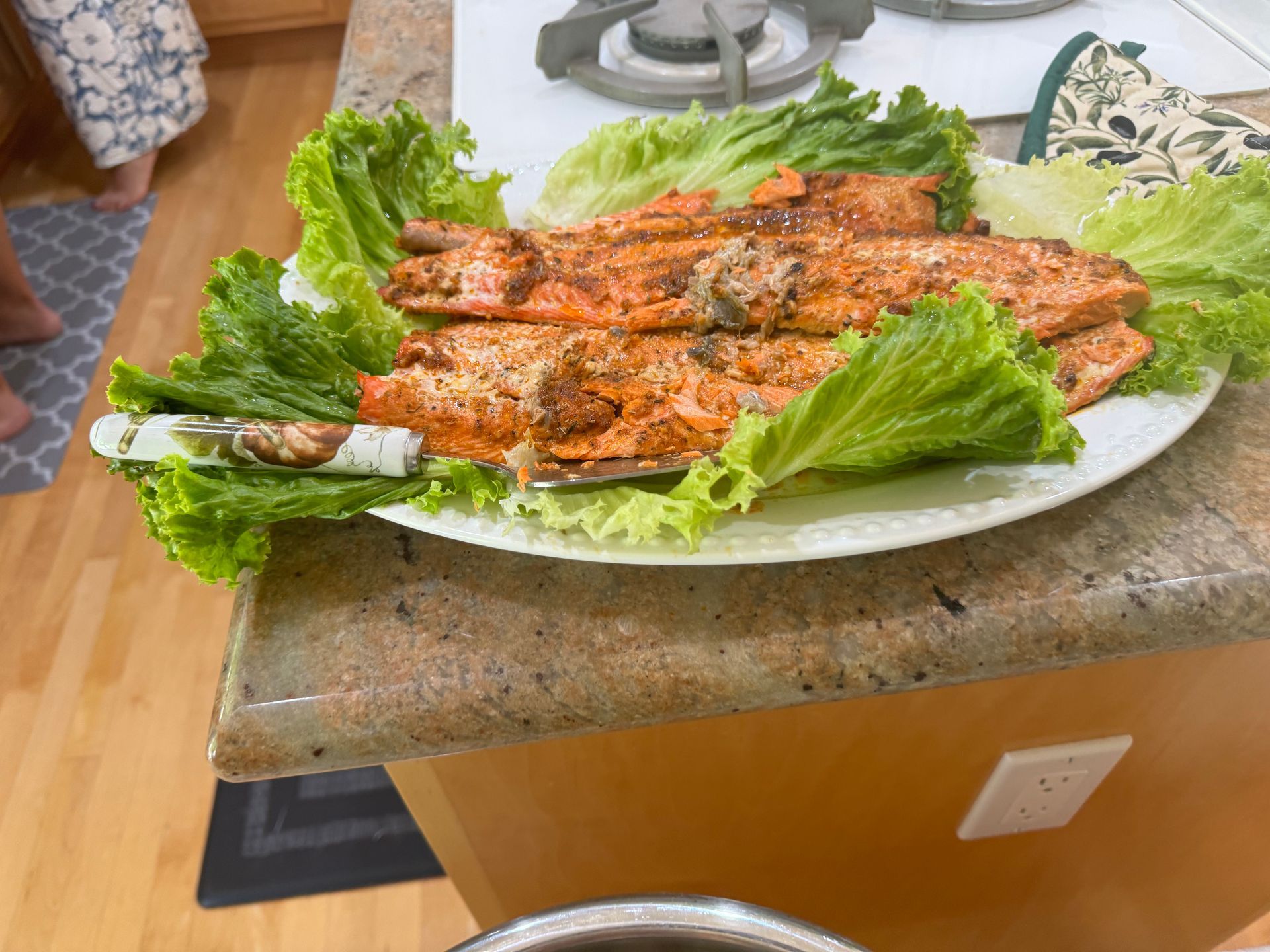 A white plate topped with salmon and lettuce on a kitchen counter.
